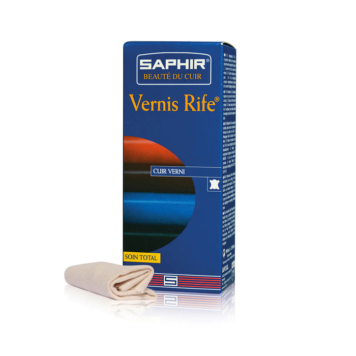 A box of Saphir Vernis Rife shoe polish with a blue and red design, alongside a cotton pad and a cloth for application.