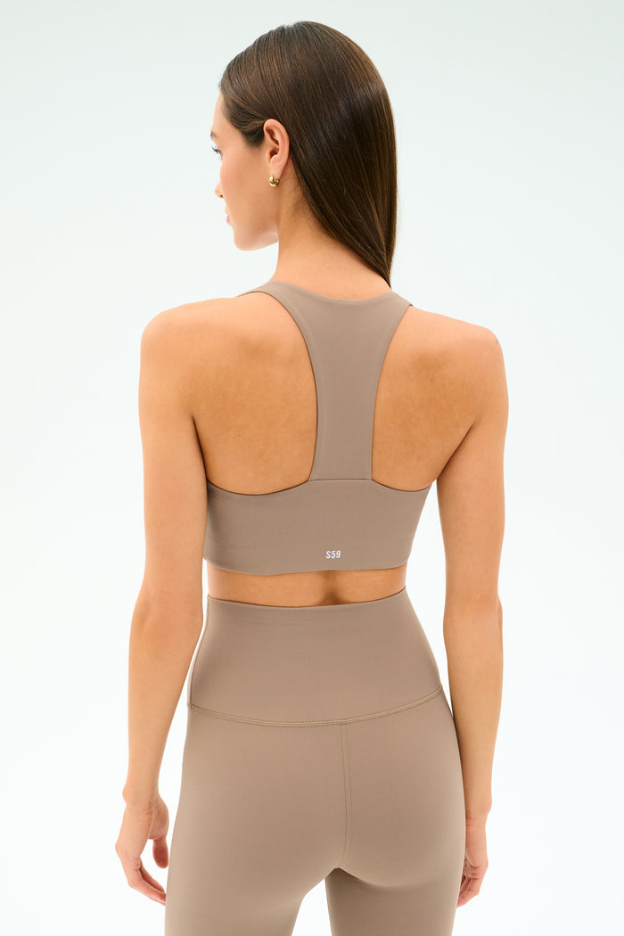 A woman is shown from the back against a plain background, wearing the SPLITS59 Sara Airweight Bra in Latte with matching high-waisted leggings—an ideal outfit for Pilates or hot yoga.