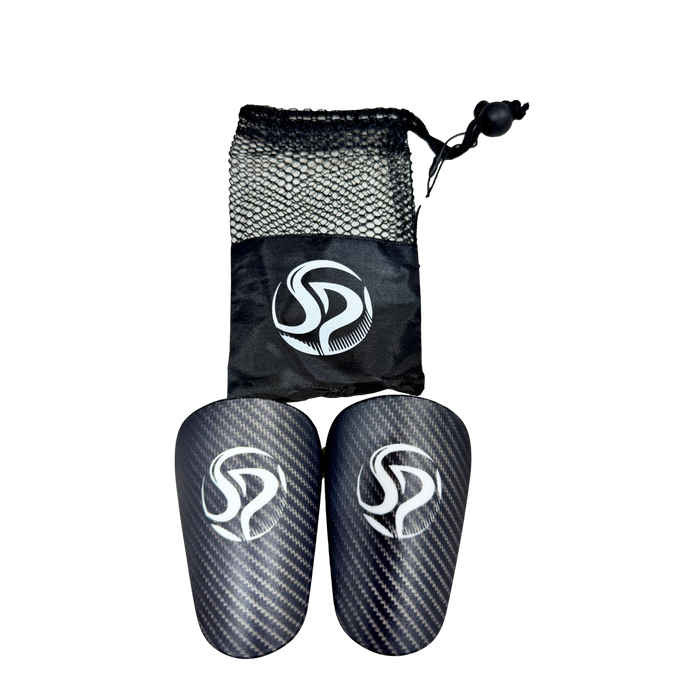 Carbon-fiber-patterned soccer shin guards and a black mesh drawstring bag, both featuring a white "SP" logo, centered on a solid black background.
