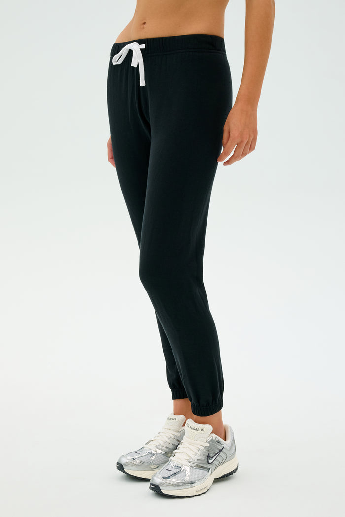A person in the Sonja Fleece Sweatpant in black from SPLITS59 and white sneakers stands against a light background.