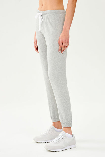 Front side view of woman wearing light grey jogger with white drawstring and white cropped tank top paired with creme shoes