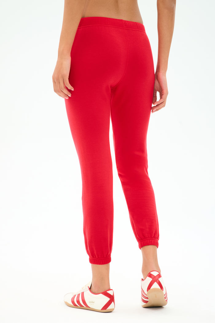 A person is shown from the back wearing SPLITS59 Sonja Fleece Sweatpant in Pirate Red with white athletic shoes featuring red stripes, standing against a plain white background—a relaxed LA-inspired look.