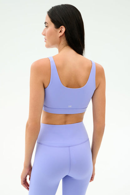 A woman faces away, wearing the SPLITS59 Sprint Rigor Bra in Purple Haze with matching high-waisted leggings—ideal for gym workouts and multi-sport performance—set against a plain light background.