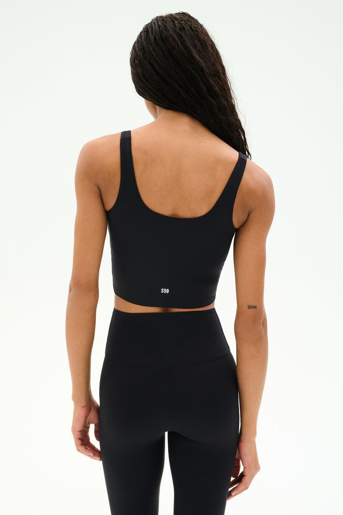 A person stands with their back to the camera, highlighting the SPLITS59 Sprint Rigor Bralette in black paired with high-waisted black leggings, set against a plain light background.