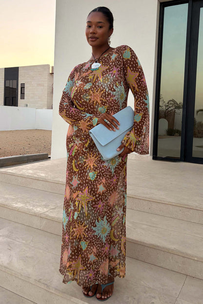 Star Fawn Aria Mesh Dress in brown with celestial star motifs and sheer flared sleeves, worn by a model with a blue clutch.