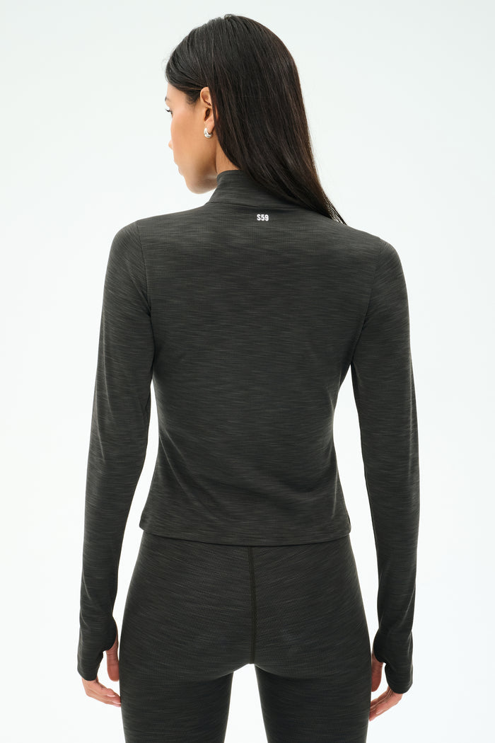 A woman facing away from the camera wears the SPLITS59 Stevie Active Rib Half Zip Waist Length top in Heather Graphite, paired with matching leggings, against a plain background.