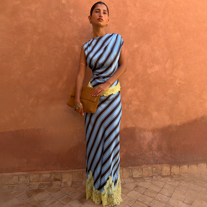Blue diagonal stripe Maeva co-ord with yellow lace detailing and asymmetric top, set against a terracotta wall.