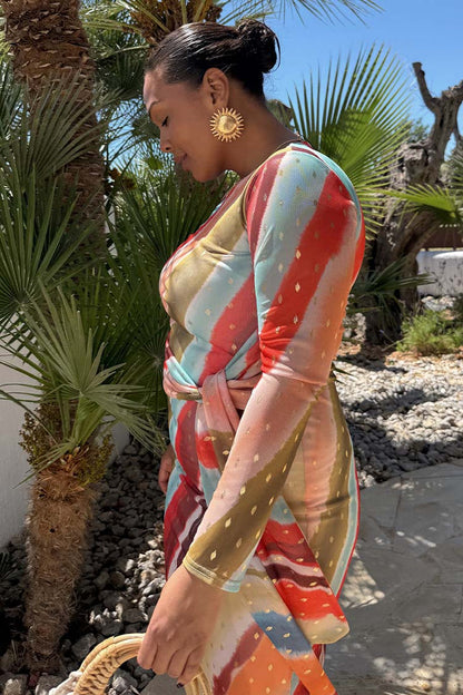 Sunset Stripe Mesh Midi Dress with a multicoloured stripe print and wrap tie waist in a vacation setting.