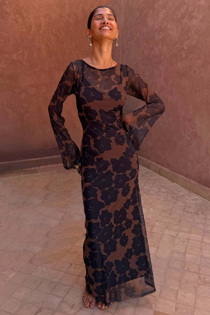 Tan Jaden Floral Mesh Maxi Dress with flared sleeves and a high neckline, worn against a terracotta background.