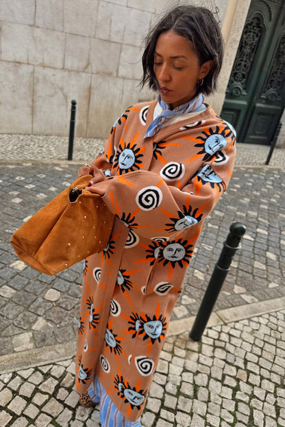 Tan Sun Cardigan with hand-painted sun motifs and dropped shoulders, styled on a cobblestone street.