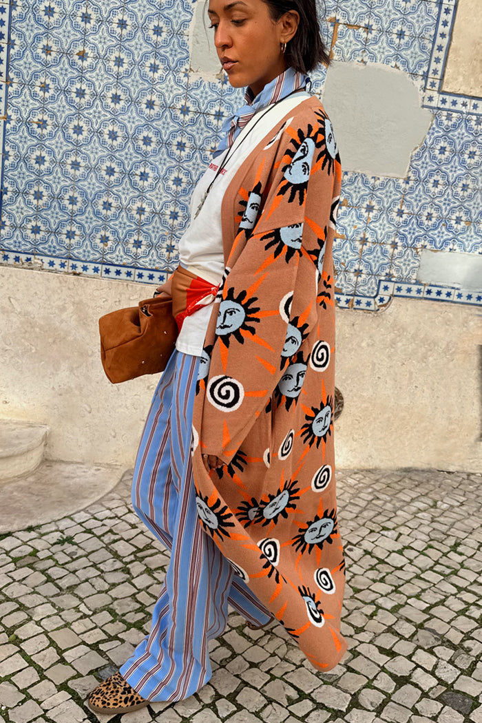 Tan Sun Cardigan with hand-painted sun motifs and an oversized fit, styled with blue striped trousers.