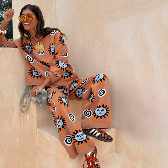 Tan Sun Trousers and matching knit jumper with sun and swirl motifs, worn by a model sitting on stone steps.