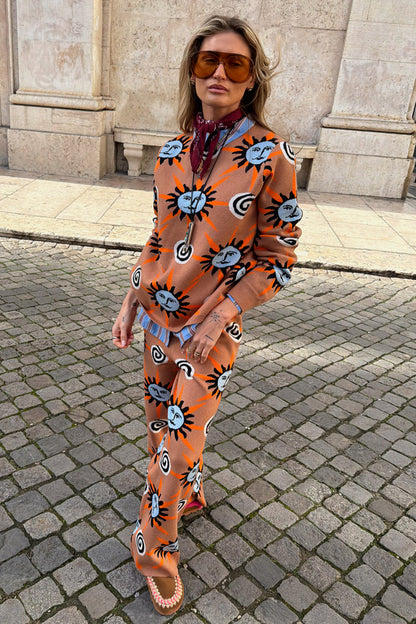 Tan Sun Trousers in a knit fabric with sun and swirl motifs, styled as a co-ord set on a cobblestone street.