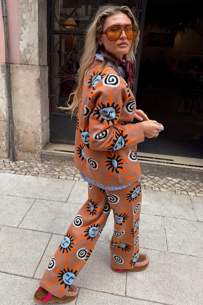 Tan Sun Trousers in a knit co-ord featuring Mediterranean sun and swirl motifs, styled on a model outdoors.