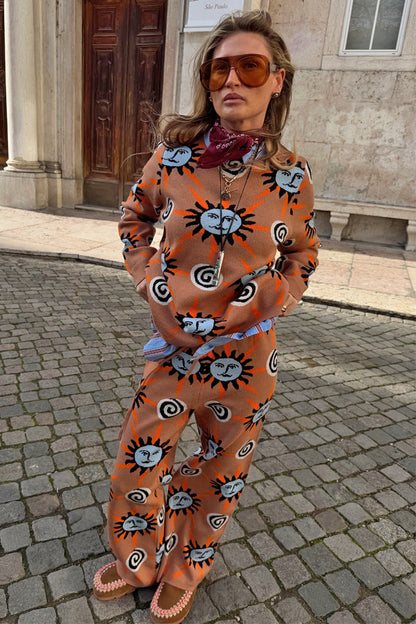 Tan Sun knit co-ord with sun and swirl motifs, styled with a bandana and sunglasses on a cobbled street.