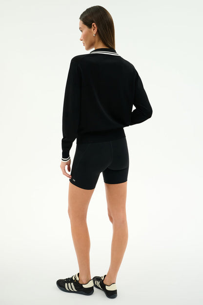 A woman stands facing away, wearing the SPLITS59 Taylor Knit Polo in Black/White against a plain white background.