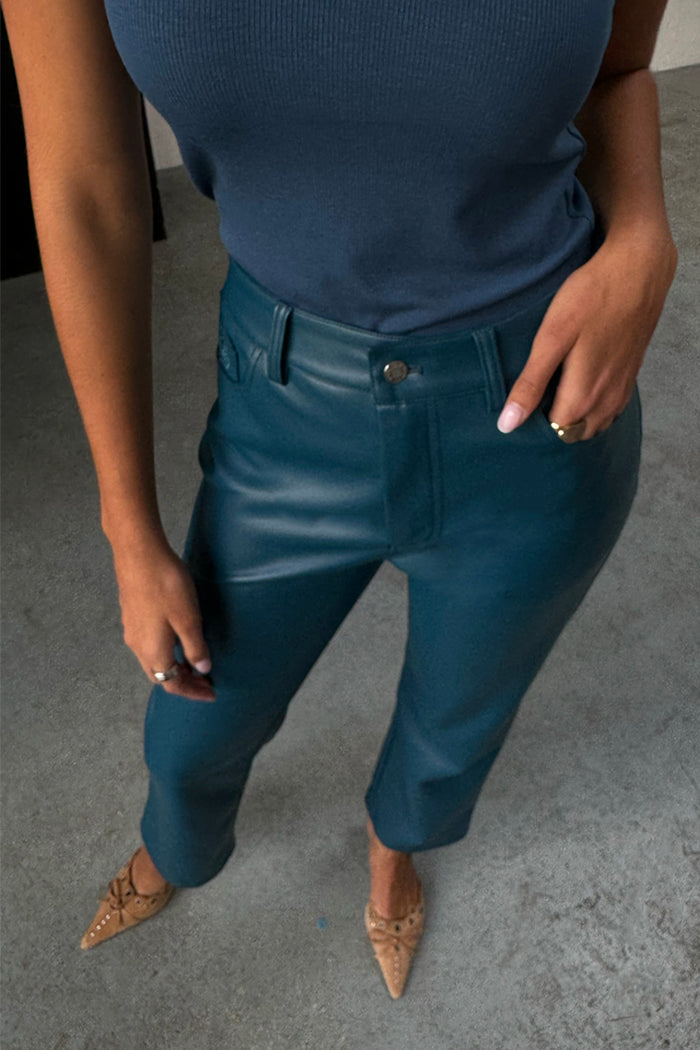 Teal Vegan Leather Trousers in a straight leg fit, styled with a blue ribbed tank top and pointed tan heels.