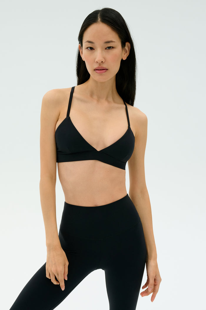 Woman stands against a plain background, wearing the SPLITS59 Theo Rigor Bra - Black and high-waisted black leggings, both crafted from ultra luxe Rigor fabric for multi-sport performance.