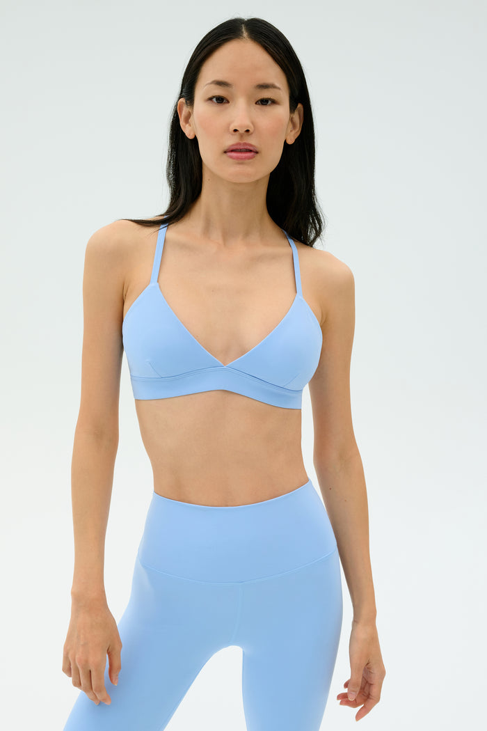 A woman stands against a plain background wearing the SPLITS59 Theo Rigor Bra in Skylight with matching high-waisted leggings.