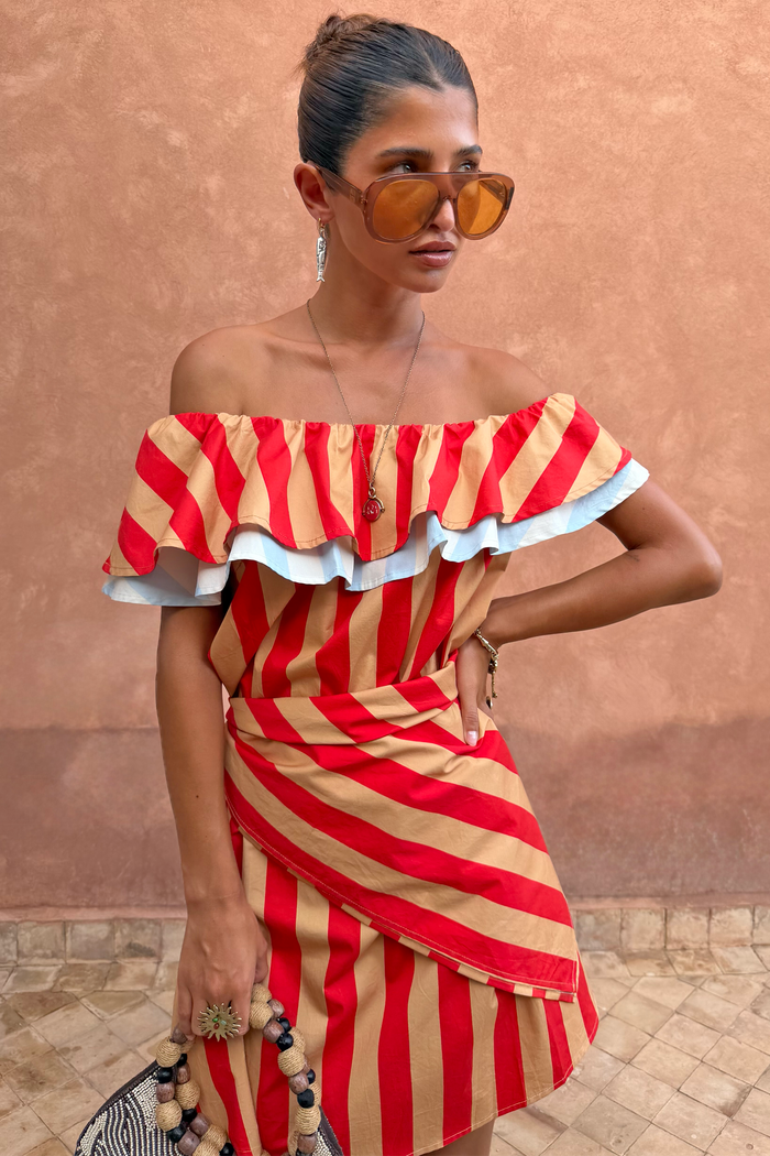 Tomato Stripe Scarf in red and tan styled as a multi-wear ruffled top against a terracotta wall.