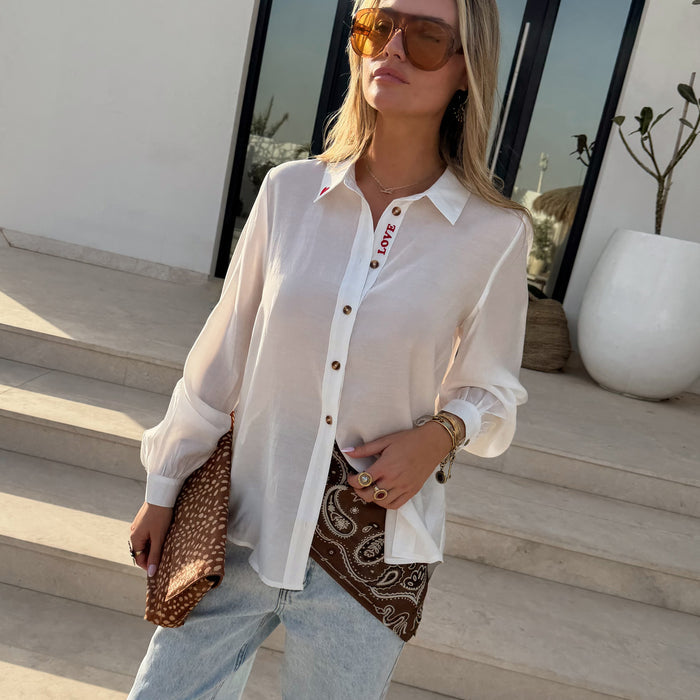 White Love Miley Shirt with sheer blouson sleeves, red embroidery and tortoise buttons, styled with jeans and a clutch.
