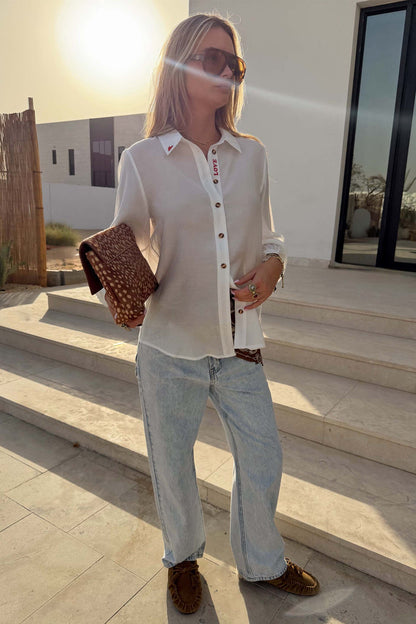 Sheer White Love Miley Shirt with heart motifs and blouson sleeves, styled with light jeans and a leopard print clutch.