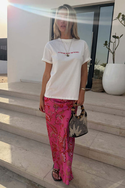 White Rodeo T-Shirt with red lettering and a relaxed fit, styled with a pink patterned skirt and a beaded bag.