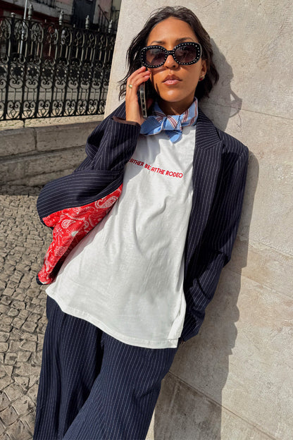 White Rodeo T-Shirt with red text, styled with a pinstripe suit and blue neck scarf for a London look.