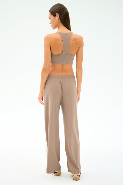 A woman stands facing away, wearing the SPLITS59 Willow Airweight Wide Leg in Latte/White with matching sports bra; her hair is down, shoes visible, against a plain light background.