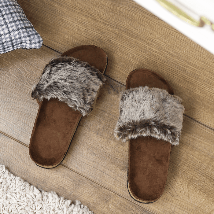Mink colour slipper sliders on wooden floor beside cushion and cream coloured rug