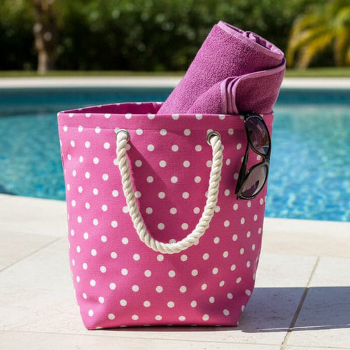Pink polka dot beach bag with a purple towel and sunglasses by a pool