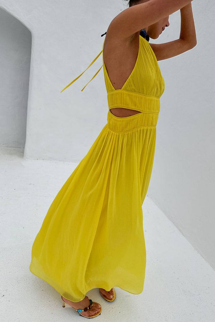 Yellow Ella Dress featuring pleated fabric, side cut-outs and a flowy midaxi silhouette against a white wall.