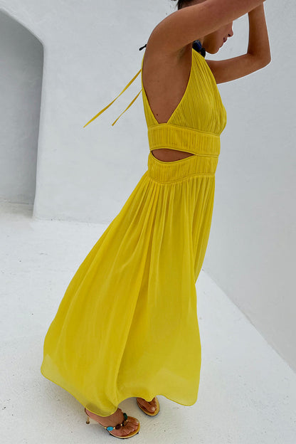 Yellow Ella Dress featuring pleated fabric, side cut-outs and a flowy midaxi silhouette against a white wall.