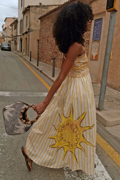 Yellow Stripe Ashley Dress featuring a large sun motif and ruffled bandeau top, captured on a sunlit street.